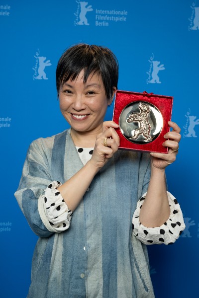 filmmaker Lesley Chan in oversized b/w top holding Golden Teddy Award