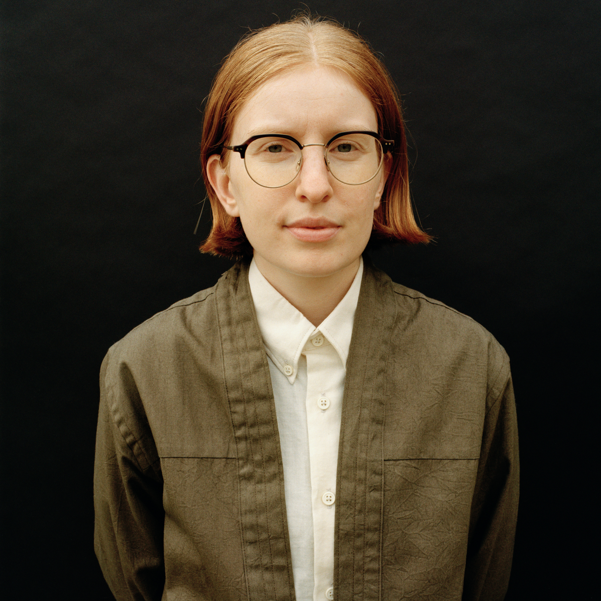 Axelle photo with shoulder-length strawberry hair, glasses, green jacket, white shirt