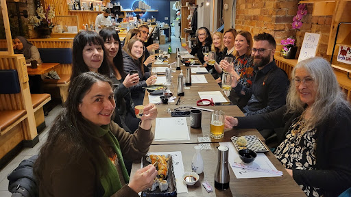 A photograph of a large group of people eating in a sushi restaurant and who are all looking toward the camera.