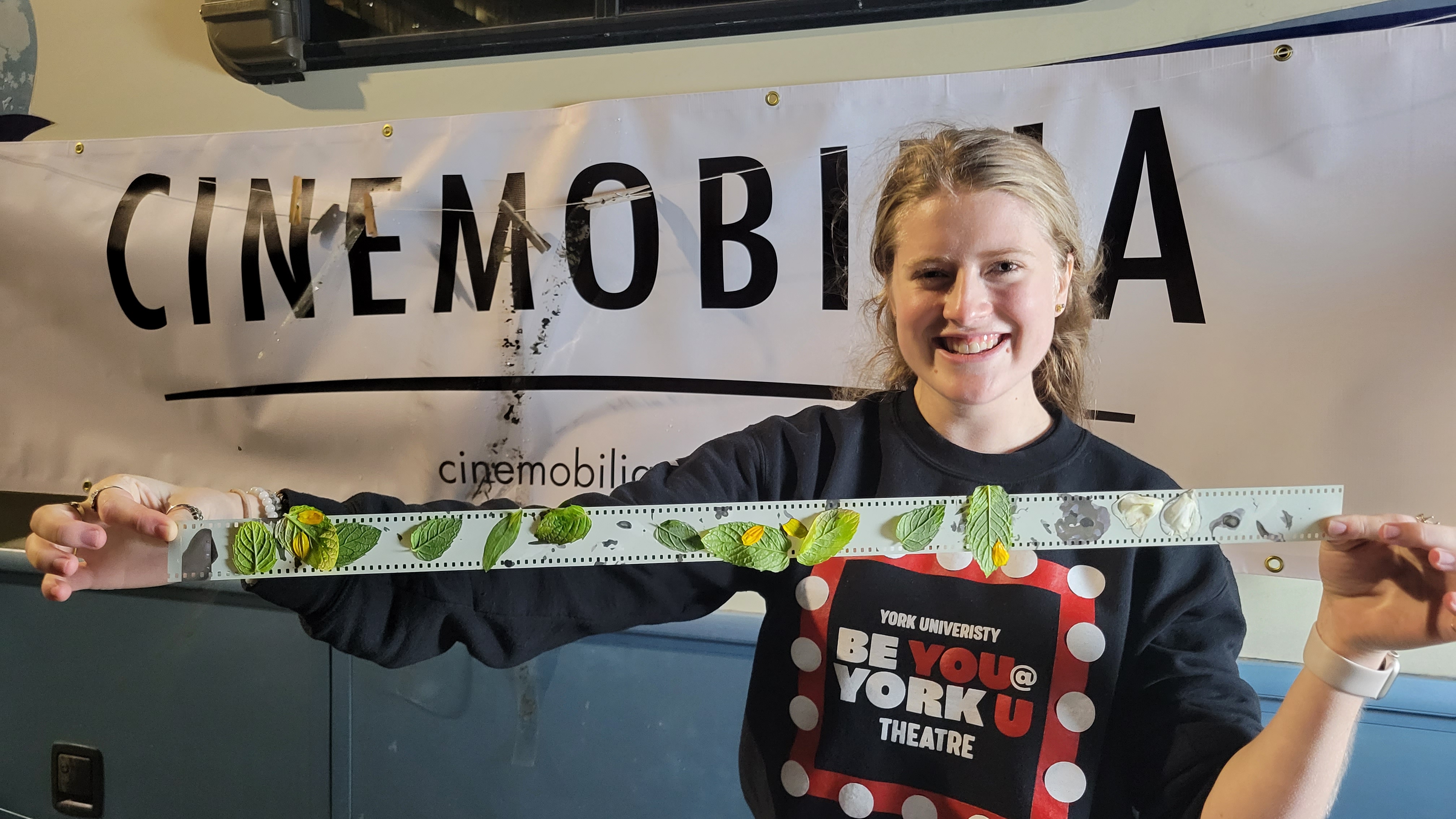 A photograph of a young woman holding up a roll of film that is covered in flower petals and leaves.