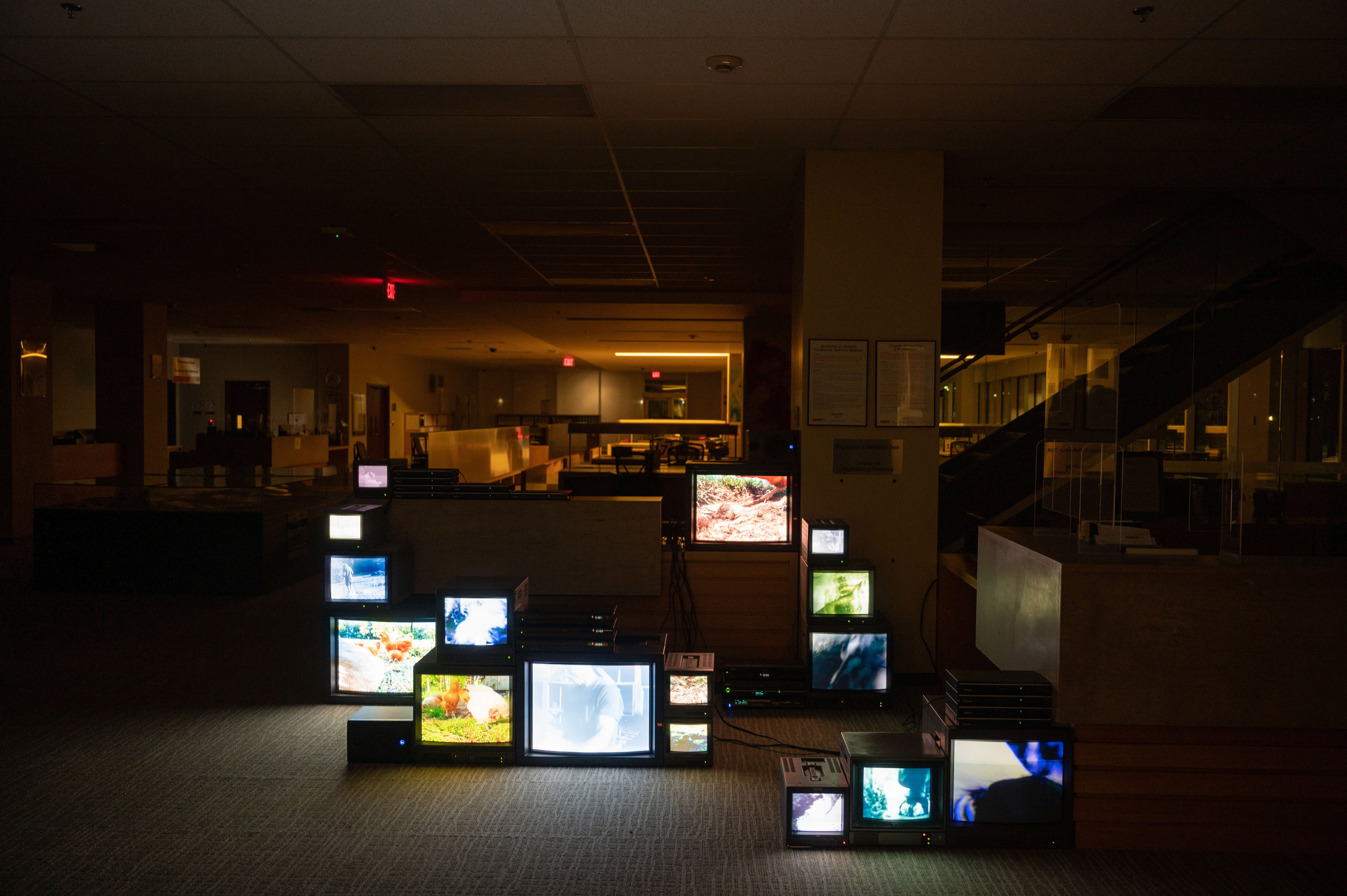 A photograph of a dark office space with a large variety of television monitors stacked on a carpeted floor.