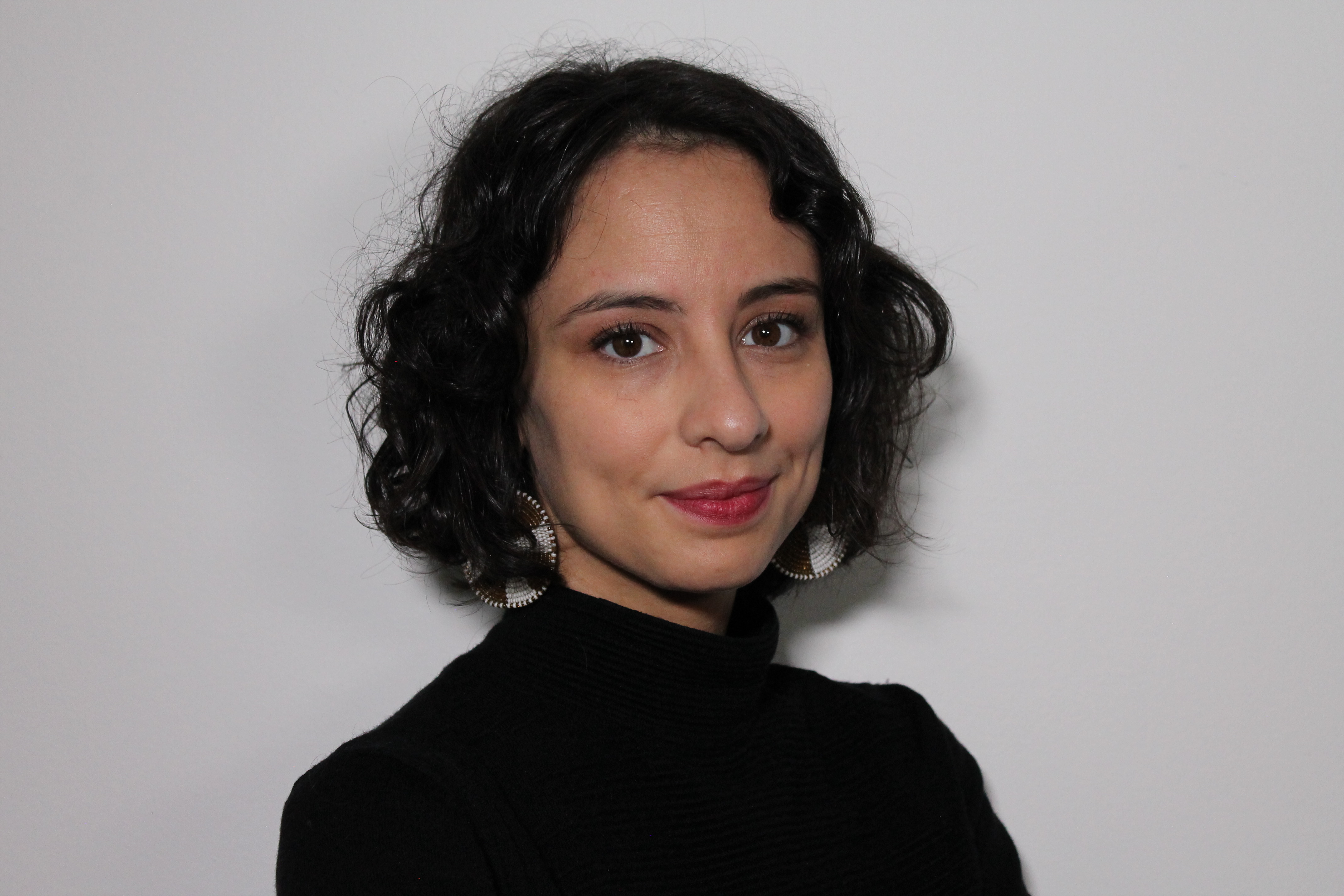 Ylenia headshot, med length dark hair, silver disc earrings, raspberry lip colour, black turtleneck