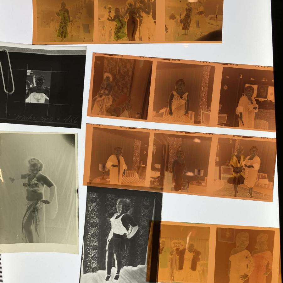 A photography of a variety of film negatives arranged on light table. All of the film negatives depict portrait photos of trans women and/or drag performers.