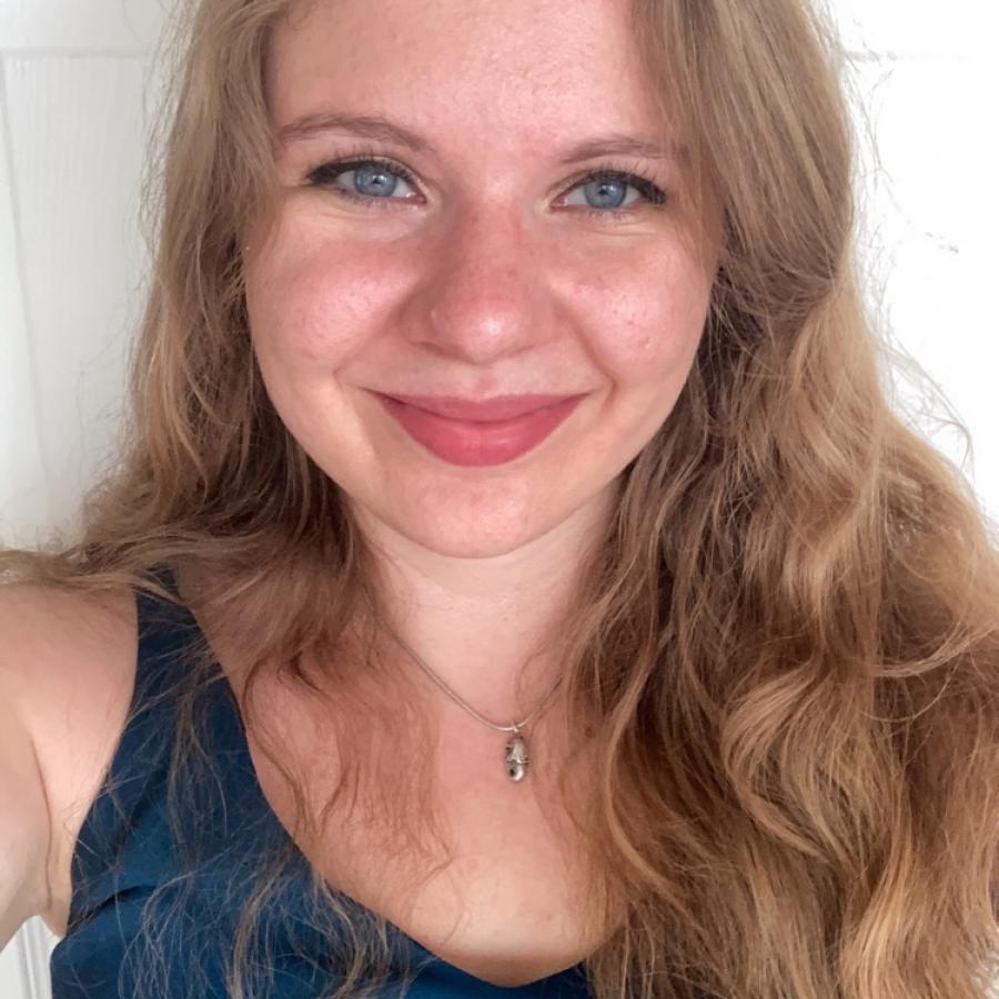 Medium shot portrait of presenter, Cate Alexander, with long blonde hair, blue eyes, a wide smile, blue sleeveless top