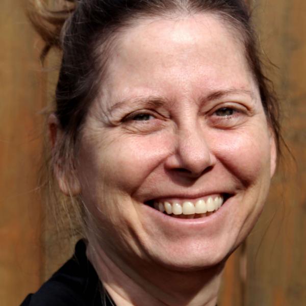 Mary Bunch is white, smiling at the camera. Her light brown hair is tied into a ponytail and she is wearing a black top.. 