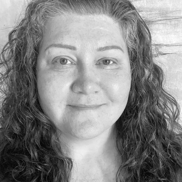 A black and white portrait photo of a smiling woman with long wavy hair standing in front of a wall with an abstract texture.