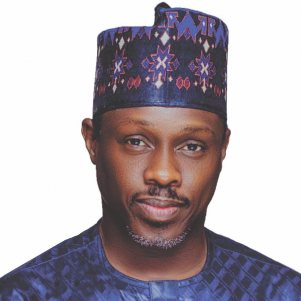 A portrait of a man in a patterned hat and shirt, looking into the camera. The image is close up, shot from the chest up. He has a slight beard and is pictured against a white background. 