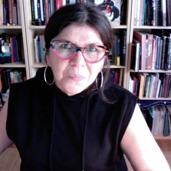 A portrait photo of a woman with black hair and glasses sitting in an office in front of a large bookcase.