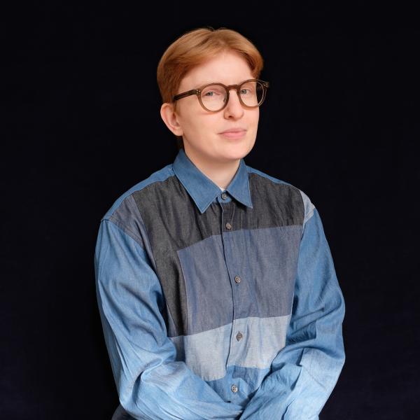 Medium shot of Axelle with short red hair, glasses, blue, long-sleeve, buttoned shirt with collar