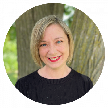 A circularly cropped portrait photograph of a smiling woman with medium-length blonde hair and a black shirt who is standing outside in front a green tree on sunny day.